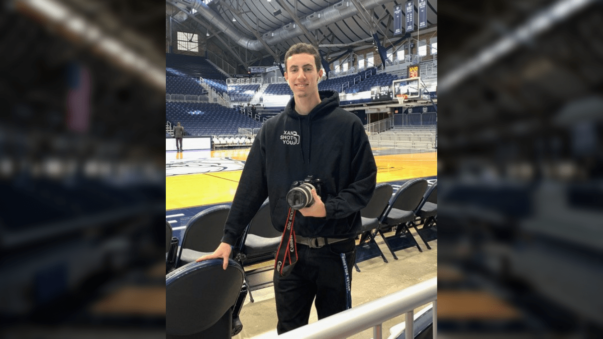 Image from Male in dark sweatshirt with words Xan Shot You, holding camera, in HInkle Fieldhouse article
