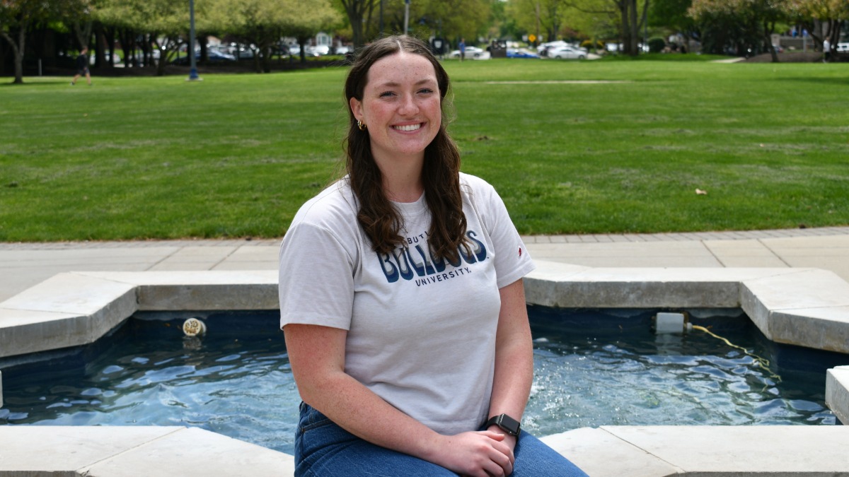 Butler student, Sarah Mangan, wearing a white Butler t-shirt and jeans, posing for a picture sitting at Star Fountain on Butler